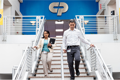 Mitarbeiter von Colgate-Palmolive gehen eine Treppe hinunter, hinter ihnen ist das Colgate-Palmolive-Logo auf einer blauen Wand zu sehen.