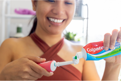Eine Frau, die lächelt, während sie im Badezimmer Colgate-Zahnpasta auf eine Zahnbürste aufträgt.